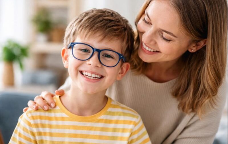 gyermek szemüvegben mosolyog, büszke anya ölelésében
