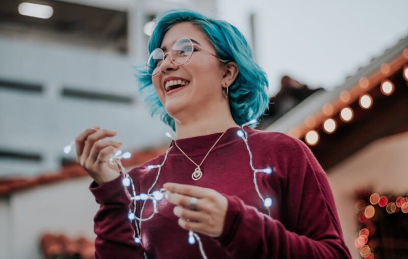 lány türkiz hajjal szemüvegben égősorral a nyakában